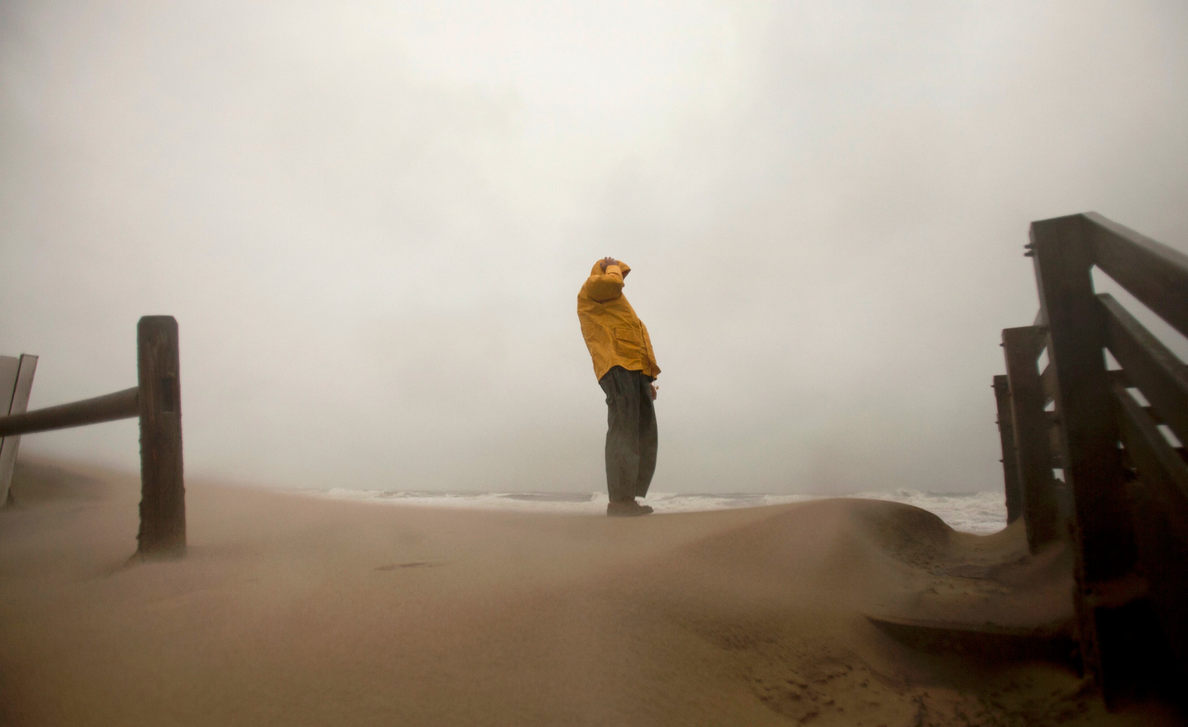 Matt Francis, of Virginia Beach, Va., holds on to his hat, as the wind-driven sand and rain from Hurricane Sandy blows across the beaches of Sandbridge in Virginia Beach, Va., Sunday Oct. 28, 2012.