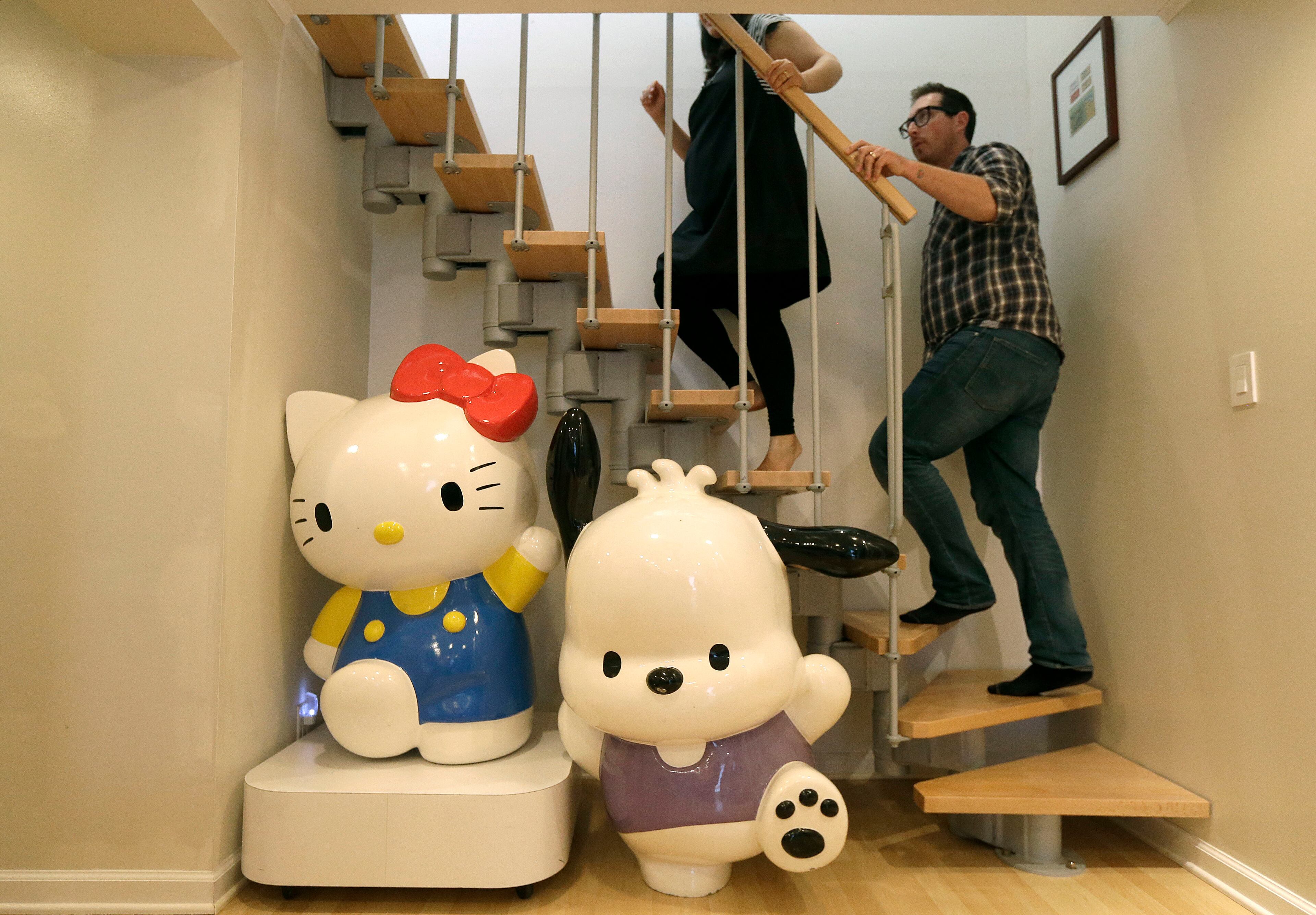 In this Monday, Oct. 13, 2014 photo, Salumeh Eslamieh, top left, and Marty Garrett walk up the stairs past statues of Sanrio characters Hello Kitty, bottom left, and Pochacco displayed at their home in San Francisco. The married couple turned the garage of their San Francisco home into a permanent showroom for their vast Hello Kitty collection. The couple met and bonded over the little white cat, and will be traveling to Los Angeles this week celebrate the character�s 40th birthday at Hello Kitty Con, opening Oct. 30, a four-day festival dedicated to all things Kitty. (AP Photo/Jeff Chiu)